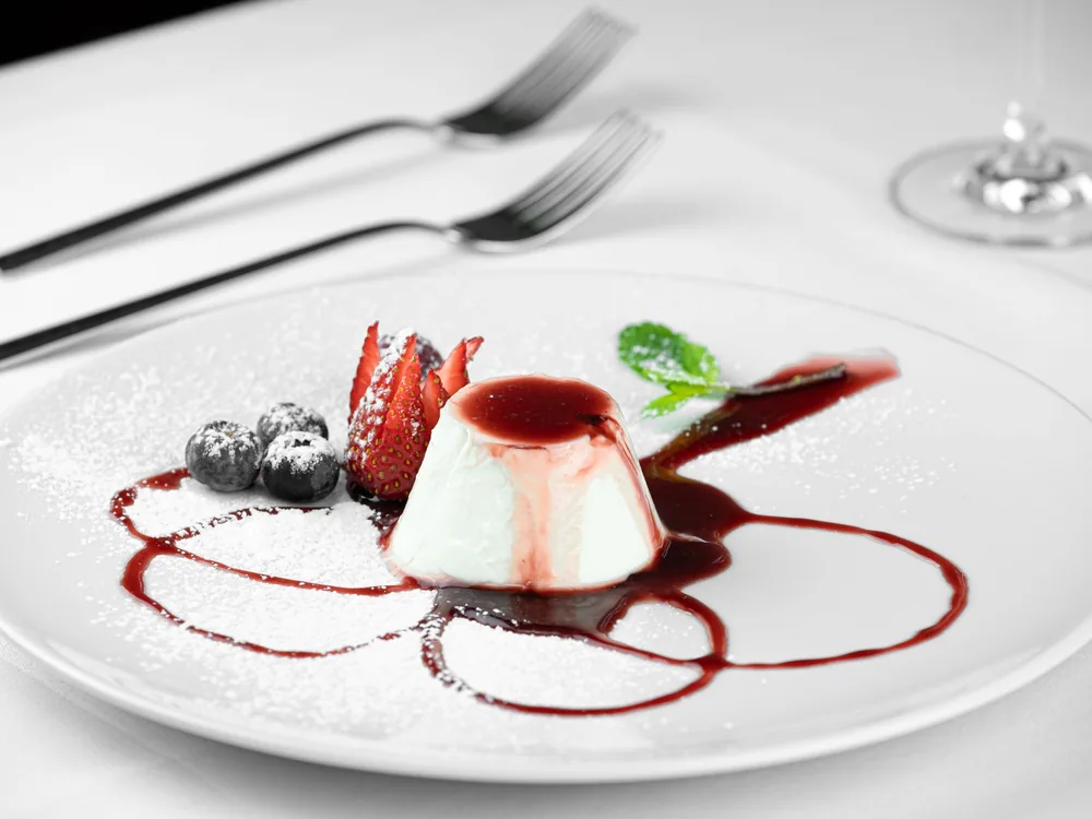 Panna cotta s čerstvým lesním ovocem a omáčkou z červených plodů na bílém talíři